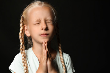 Little girl praying on dark background