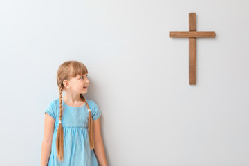 Little girl near light wall with cross