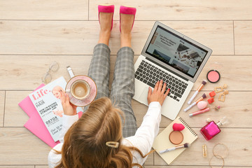 Female beauty blogger with laptop and cup of coffee sitting on wooden floor, top view