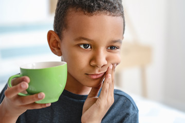 Little African-American boy with sensitive teeth and cup of tea at home