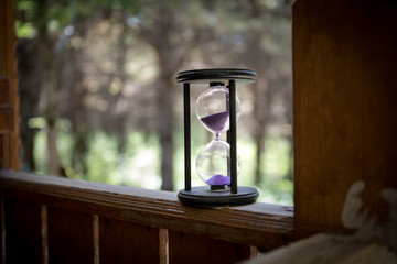 Sand running through the bulbs of an hourglass measuring the passing time in a countdown to a deadline, on a colorful background with copy space. Abstract old sand-glass in forest.