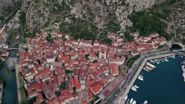 Overhead aerial view of rooftops and streets in historic old town of Kotor and Dobrota and bay for liner and boats in Montenegro in 4k