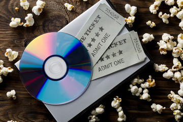 Movie tickets, DVD or blu ray disc and popcorn on dark wooden table background. Home theatre movie...