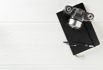 Retro analog film camera with notebook and pen on white wood table background with copy space - photography, journalism, blogging or creativity concept, flat lay top view from above