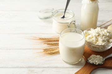 Spikelets of wheat, dairy products and board on white wood background, copy space