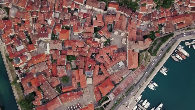 Overhead aerial view of rooftops and streets in historic old town of Kotor and Dobrota and bay for liner and boats in Montenegro in 4k