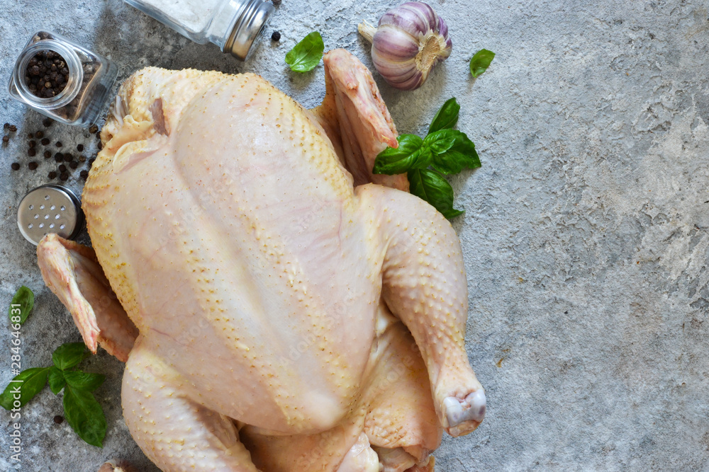 Wall mural Fresh, raw chicken with spices and basil on the kitchen table. View from above.