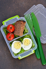 Lunch box with egg, tomato, salad and sandwich. View from above.
