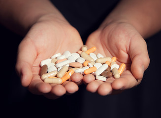 Kid holds stack of colorful pills and drugs in his palms on dark moody background. Concept of drug addiction and suicide.