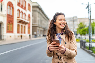 Photo of a woman using smart phone. Beautiful woman texting on the street. Beautiful woman spending...