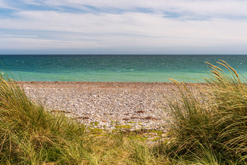 Summer Irish scene on a wild pebble beach with turquoise water and tall marram grass. Summertime leisure concept.