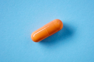 Macro view of orange colored medical pill capsule on blue background
