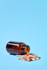 Pills spilling out of medical drug bottle on blue background with copy space