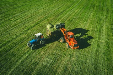Aerial view of tractor with round baler rolling bales of straw on harvested field