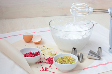 Preparation of meringue with pistachio and raspberry in a glass bowl. White textile towel and waxed paper on background. Day light