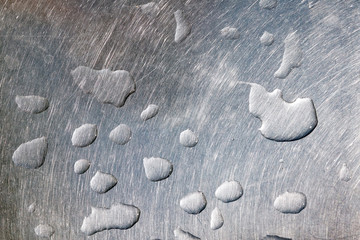 Water droplets on a scratched and worn stainless steel metal surface under natural light