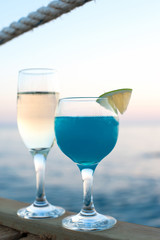 Two glasses with champagne and fresh blue cocktail at sunset