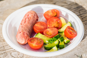 Salad of red tomatoes and green cucumbers with sausage are on plastic plate.