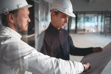 Builder worker and safety inspector wearing helment have meeting while look on construction...
