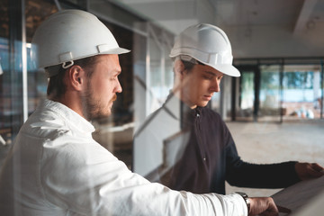 Worker and engineer have meeting while look drawing building under constuction. Two building engineers wearing safety hard hat discussing blueprint on construction site