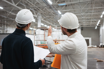 Architect and builder look on blueprint building under construction. Engineer and worker wearing...