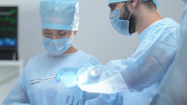 Female nurse and male surgeon taking cotton swab by forceps in operating room