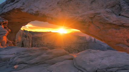 Cliff's-edge sandstone Mesa Arch framing an iconic sunrise view of the red rock canyon landscape below