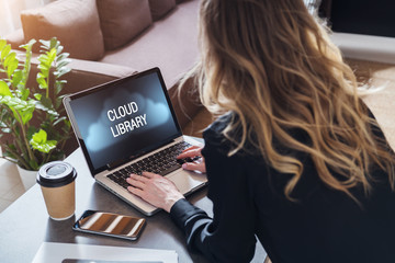 Back view of woman is working on laptop computer with inscription on monitor- cloud library.Online education, e-learning.