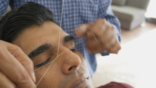 Eyebrows depilation with a thread in close-up. Threading, method of facial hair removal in a beauty parlor. Skillful beautician makes threading hair removal procedure.