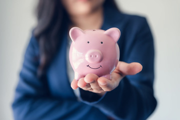 Fototapeta na wymiar Business Woman Investor Holding Piggy Bank for Money Savings on Her Hands, Asian Businesswoman in Uniform Suit Showing Money Saving While Looking at Camera., Investment and Financial Concept.