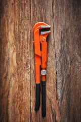 Heavy-duty orange pipe wrench on vintage wooden table under dark dramatic moody lighting.