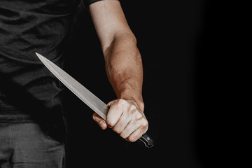Man's hand holds a knife on black background. topics of violence and murder. thief, killer, rapist,...