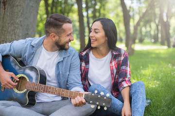 guy and girl play the guitar in the park, sit on the grass near the tree