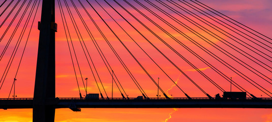 Trailer and pickup truck drives across the suspension bridge at dusk.