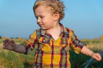 Little fair-haired boy playing on a wheat field with bales