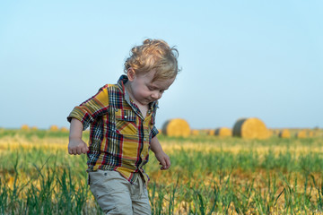 Naklejka na ściany i meble Little boy playing on a wheat field with bales
