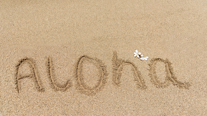 Fototapeta na wymiar Aloha, the traditional Hawaiian greeting, written in the sand of a Hawaiian beach, with a traditional Frangipani flower