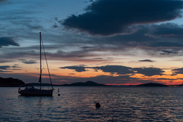 Ankernde Segelyacht in einer Bucht im Mittelmeer bei wolkigem, dramatischen Sonnenuntergang
