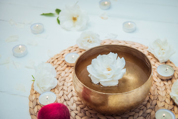 Obraz na płótnie Canvas Tibetan singing bowl with floating in water rose inside. Special sticks, burning candles, flowers petals on the white wooden background. Meditation and Relax. Exotic massage. Copy space.