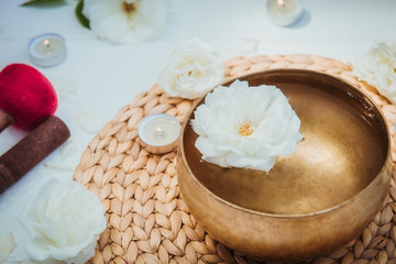 Tibetan singing bowl with floating in water rose inside. Special sticks, burning candles, flowers petals on the white wooden background. Meditation and Relax. Exotic massage. Copy space.