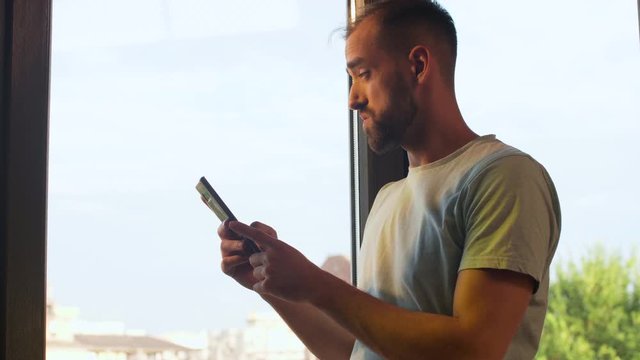 Unicorn start up company manager looking at his phone near a big window in the office. Beautiful warm light is hitting his face