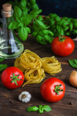 fresh tomatoes basil garlic olive oil glass bottle raw pasta fettuccine on wooden background vertical close up