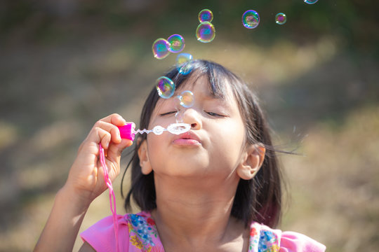 Cute little Asian girl playing soap bubbles at park, outdoors
