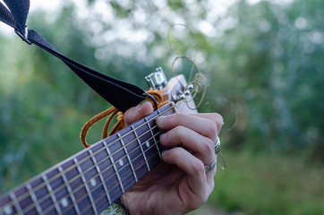 The guy plays on the street in the open air on an acoustic guitar. Fingers hold the accord B7 (H7)....