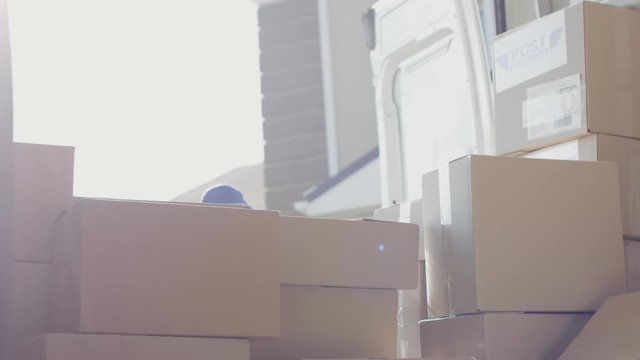 Handheld shot from inside of mail van: young female courier in blue cap looking for clients package, then picking up box for delivery