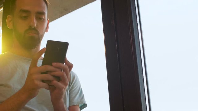 Handheld shot of manager looking at the phone in warm sunset light near a window in the office. Slow motion shot