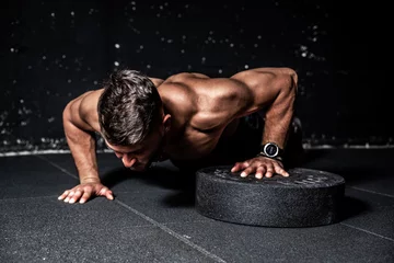 Fotobehang Young strong sweaty focused fit muscular man with big muscles performing push ups with one hand on the barbell weight plate for training hard core workout in the gym  © Srdjan