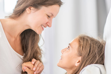 Happy mother talking with her little girl before bedtime at home