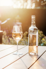 Cold rose wine in bottle and glass on table in garden at sunset light. Sun reflecting in wine glass. Backyard outdoor summer lifestyle.