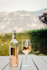 Cold rose wine in bottle and glass on table in garden with mountain view at background.  Backyard...